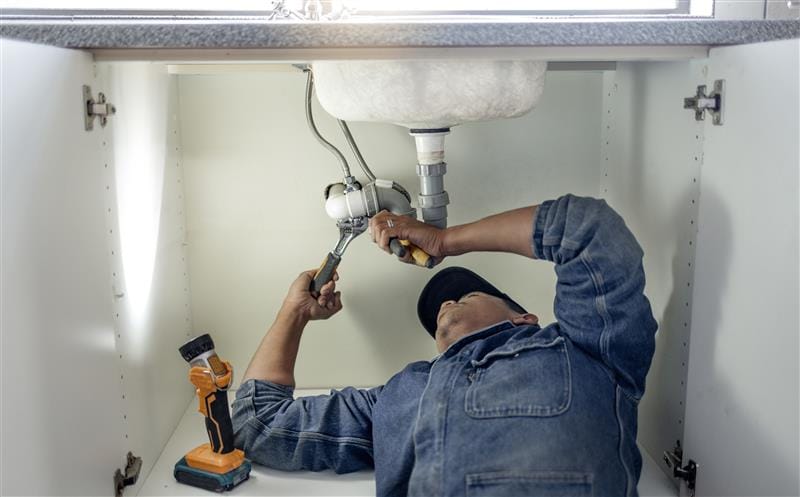 Plumber repairing pipes beneath a bathroom sink in Rancho Palos Verdes